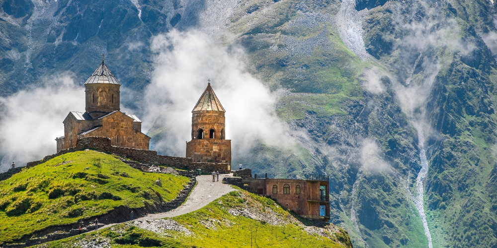 Majestic church on a green hillside with mountains in the background, a perfect backdrop for outdoor adventures.