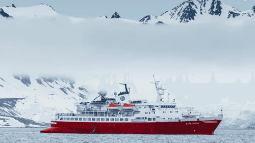Red expedition cruise ship sailing past snow-covered mountains on the Atlantic Expedition Cruise - Iceland, Greenland, Labrador route.