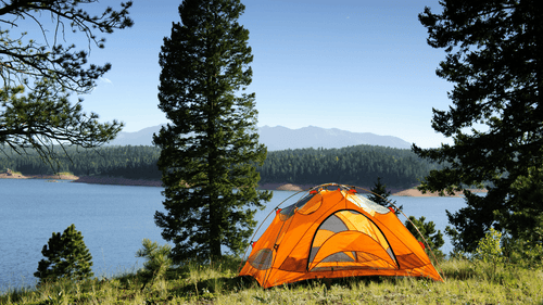 Orange camping tent near lake with forest and mountain views on Yellowstone Grand Teton 6-Day Tour - Experience Geysers & Wildlife.