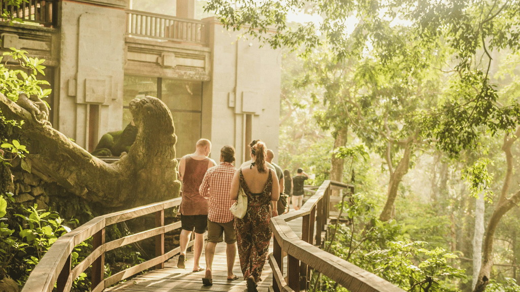 Tourists walking through forest boardwalk near sculptures, part of the immersive Soul of Sulawesi - Tana Toraja Culture Tour.