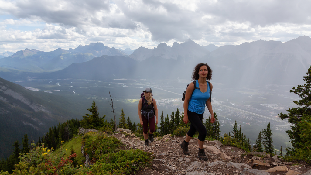 Two women hiking a mountain trail with panoramic views on the Vancouver Calgary Rockies Tour - 14 Days | Scenic Travel. Perfect for adventure seekers.