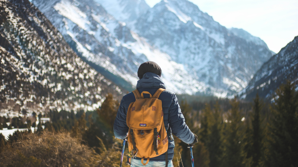 Winter hiker with poles and backpack facing snowy fjords in Northern Québec. Part of 7-day lodge escape with forest trails and scenic views.