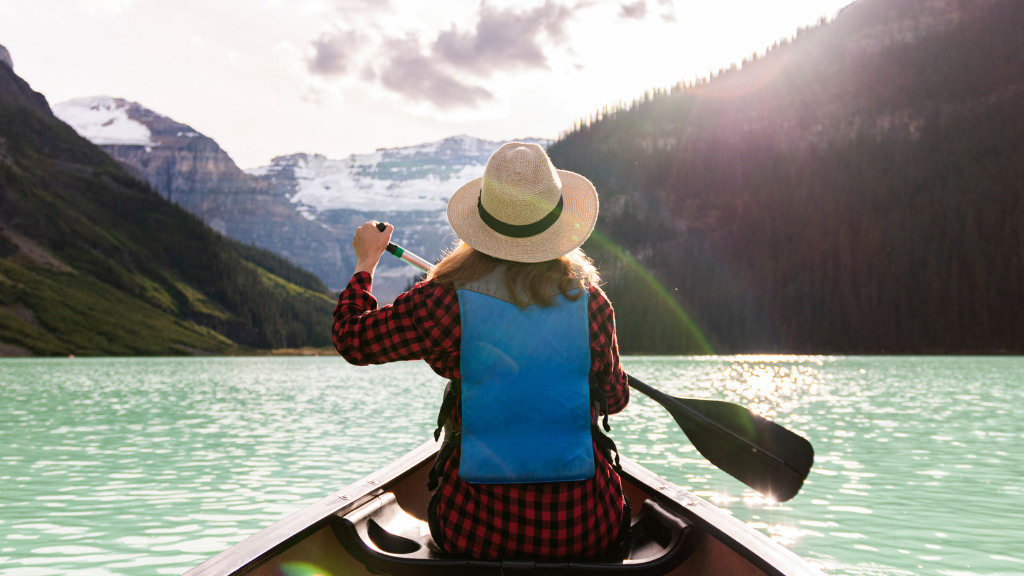 Woman paddling a canoe on a glacier-fed lake during the Explore Rockies 8-Day Tour - Scenic Peaks | Hotel Stays. Perfect for family-friendly adventure and scenic views.