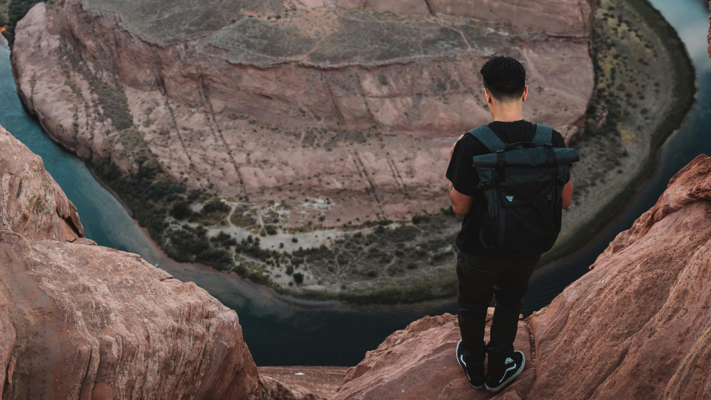 Man stands on cliff edge overlooking Horseshoe Bend in Arizona. Discover Western USA trips with canyon adventures and scenic overlooks.