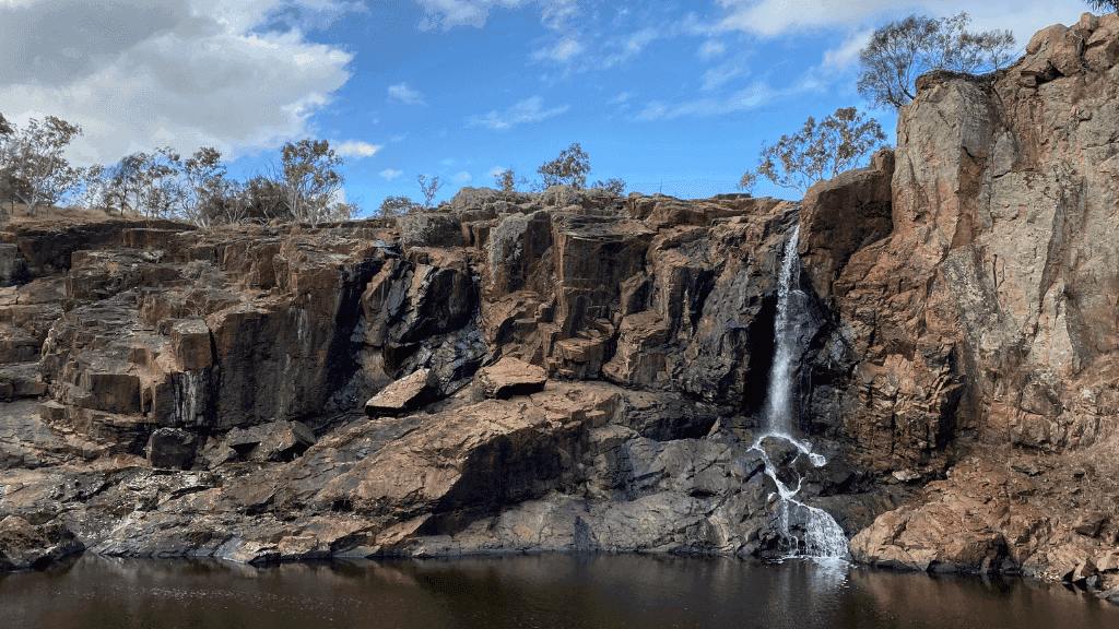 Waterfall cascading down rugged cliffs in a serene outdoor landscape, showcasing nature's beauty.