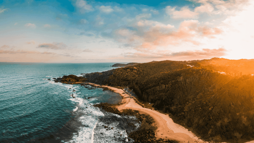 Aerial view of Tasmania's rugged coastline at sunset, showcasing remote beaches and forested cliffs on the 7-day kayak expedition route.