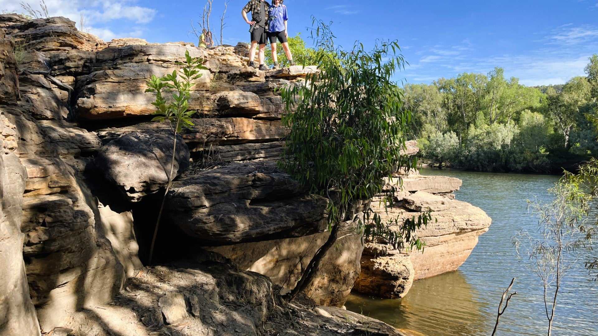 Hikers explore rocky riverbank on Kakadu Katherine Gorge Tour | 4-Day Comfort Travel. Outdoor adventure in scenic gorge setting.