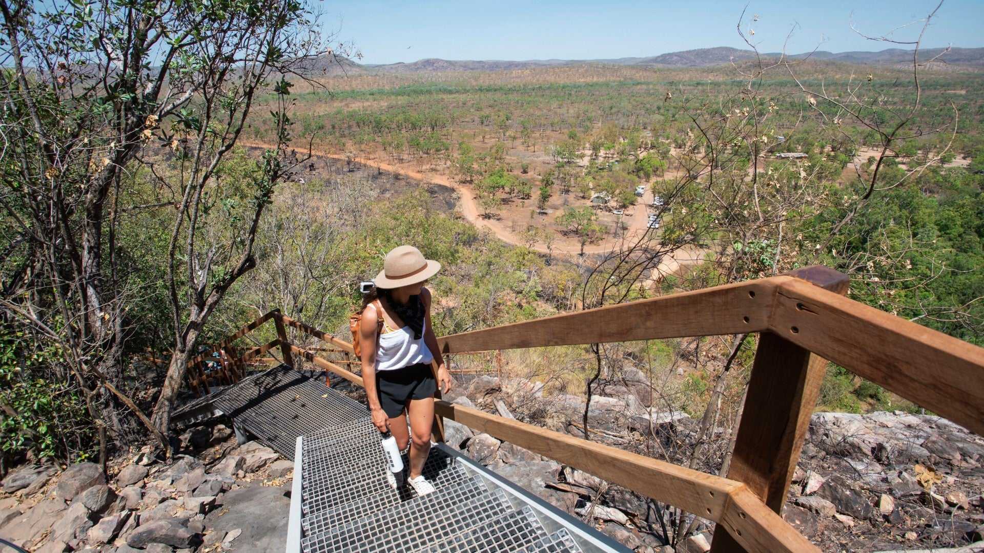 Woman hiking up lookout stairs at Kakadu Litchfield Camping Adventure - 3-Day Tour. Elevated view of dry savannah and rugged terrain.