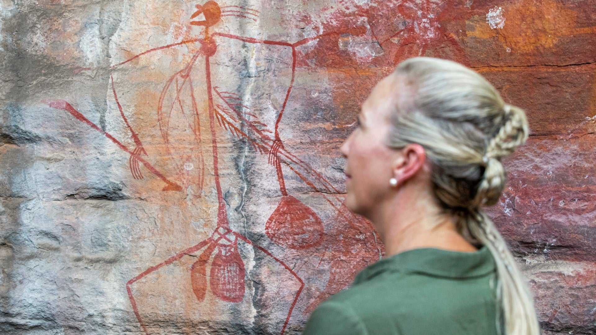 Woman observes ancient Aboriginal rock art on Kakadu Katherine Gorge Tour | 4-Day Comfort Travel. Cultural appreciation in natural setting.
