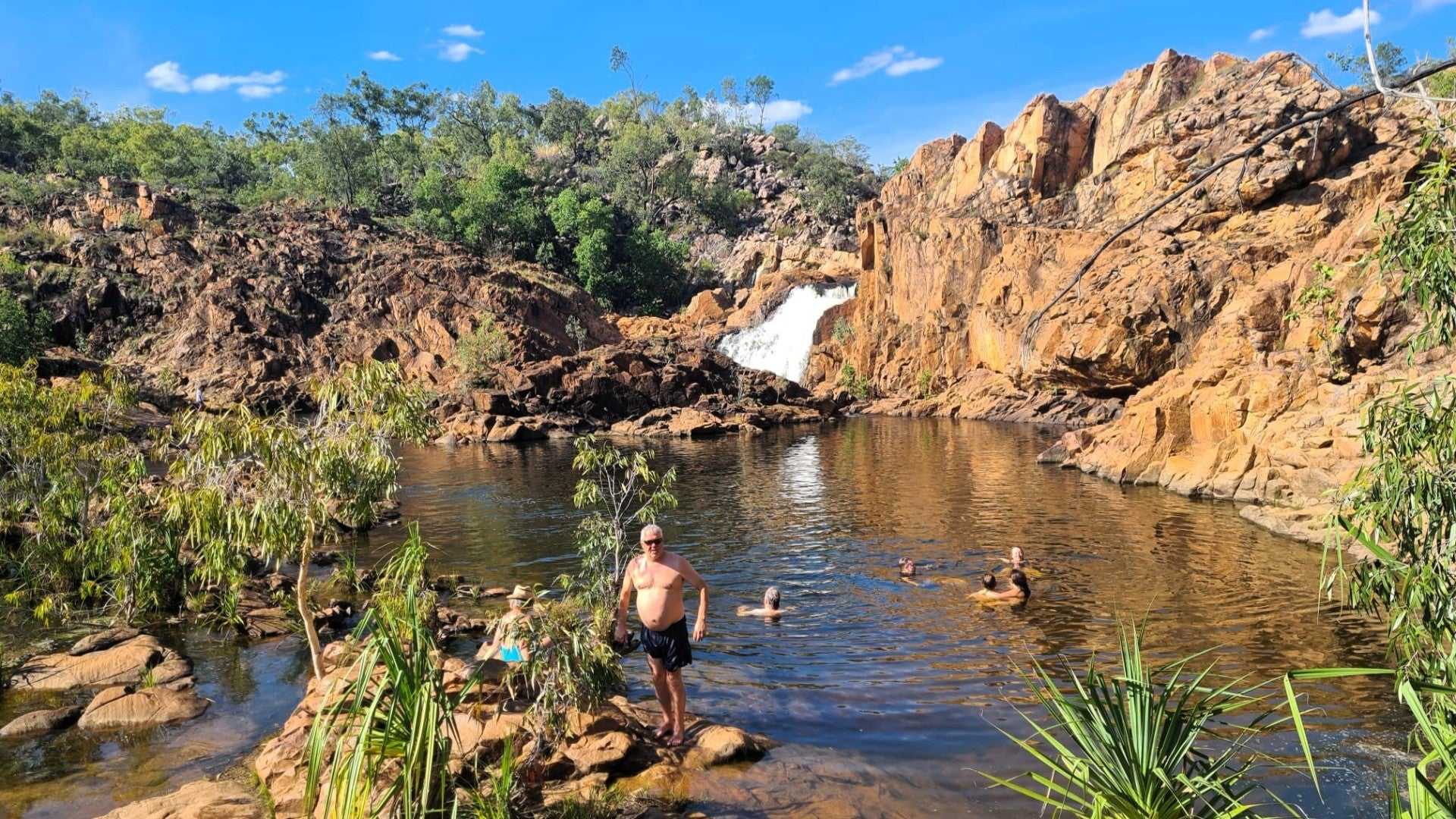 Tourists swim in natural pool below waterfall on Kakadu Katherine Gorge Tour | 4-Day Comfort Travel. Refreshing break in scenic gorge.