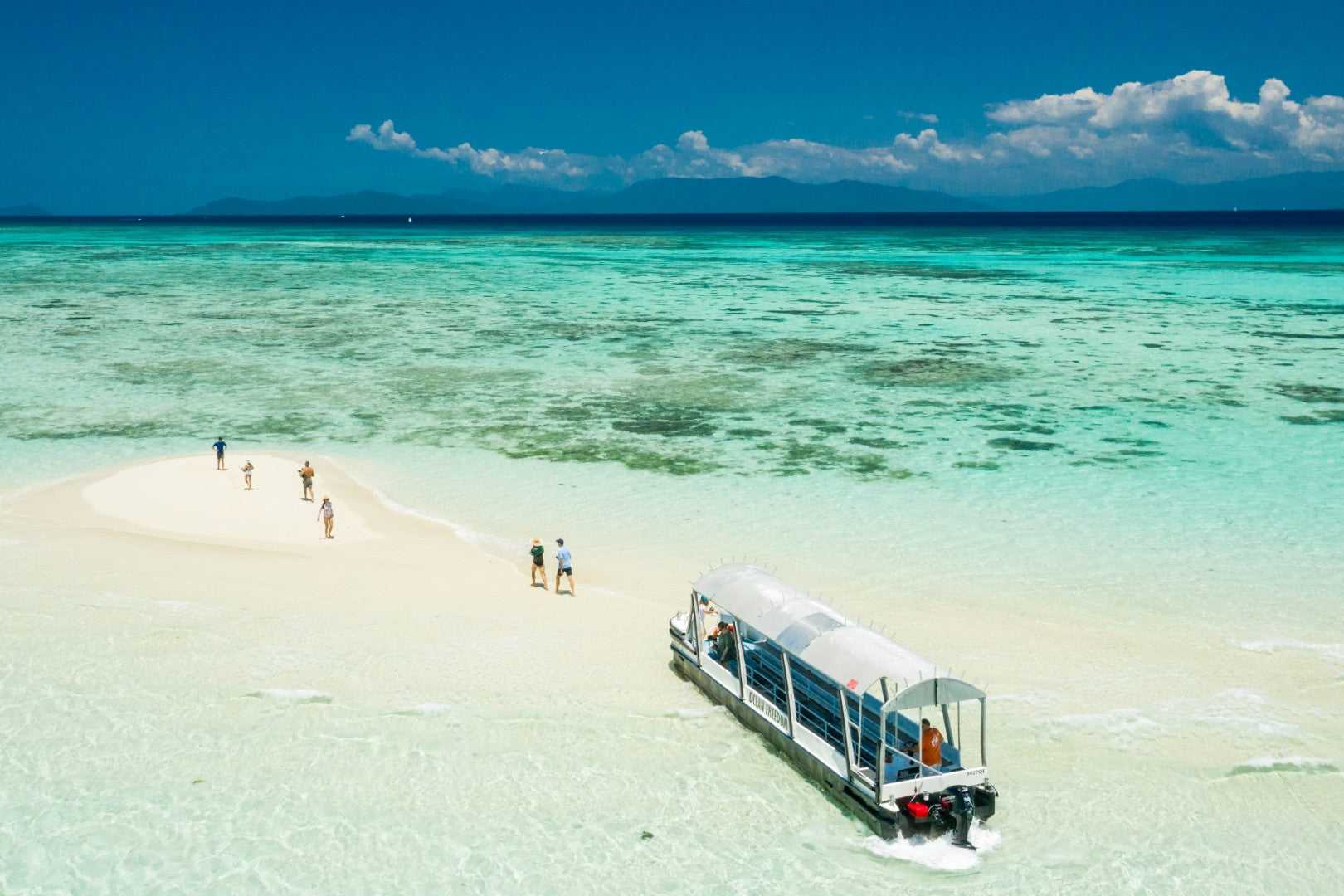 Glass-bottom boat arrives at coral cay in the Great Barrier Reef, featured on the Whitsundays Reef Tour from Brisbane to Cairns.