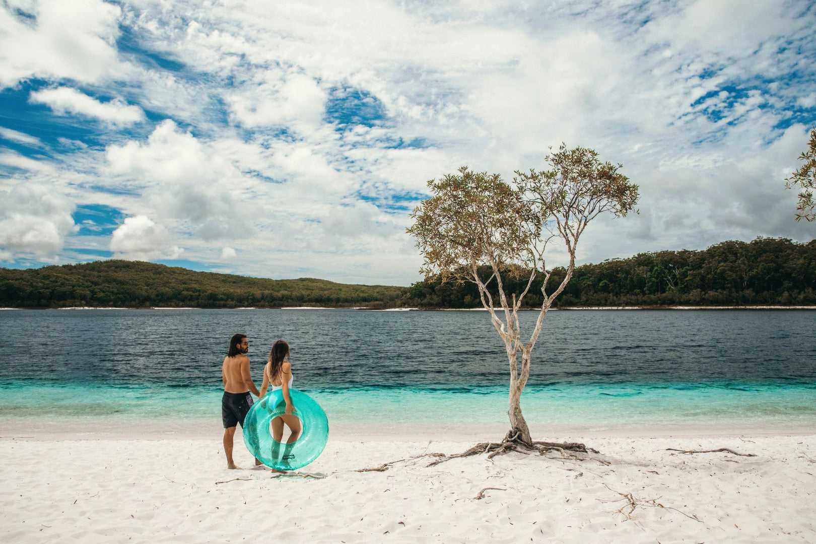 Couple with float at Lake McKenzie on K'gari during 8-day East Coast Australia tour. Scenic beach stop from Sydney to Brisbane travel route.