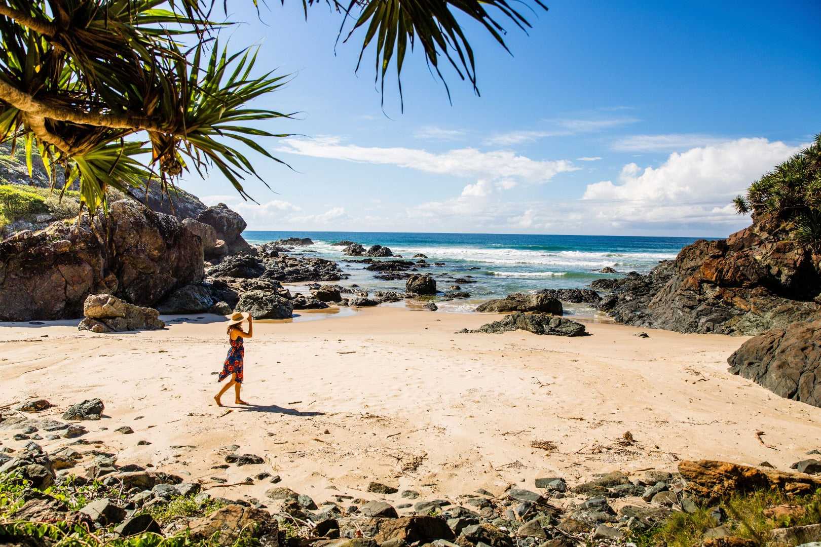 Woman walking on secluded beach with rocky coastline on East Coast Australia tour. Scenic stop on 8-day Sydney to Brisbane itinerary.