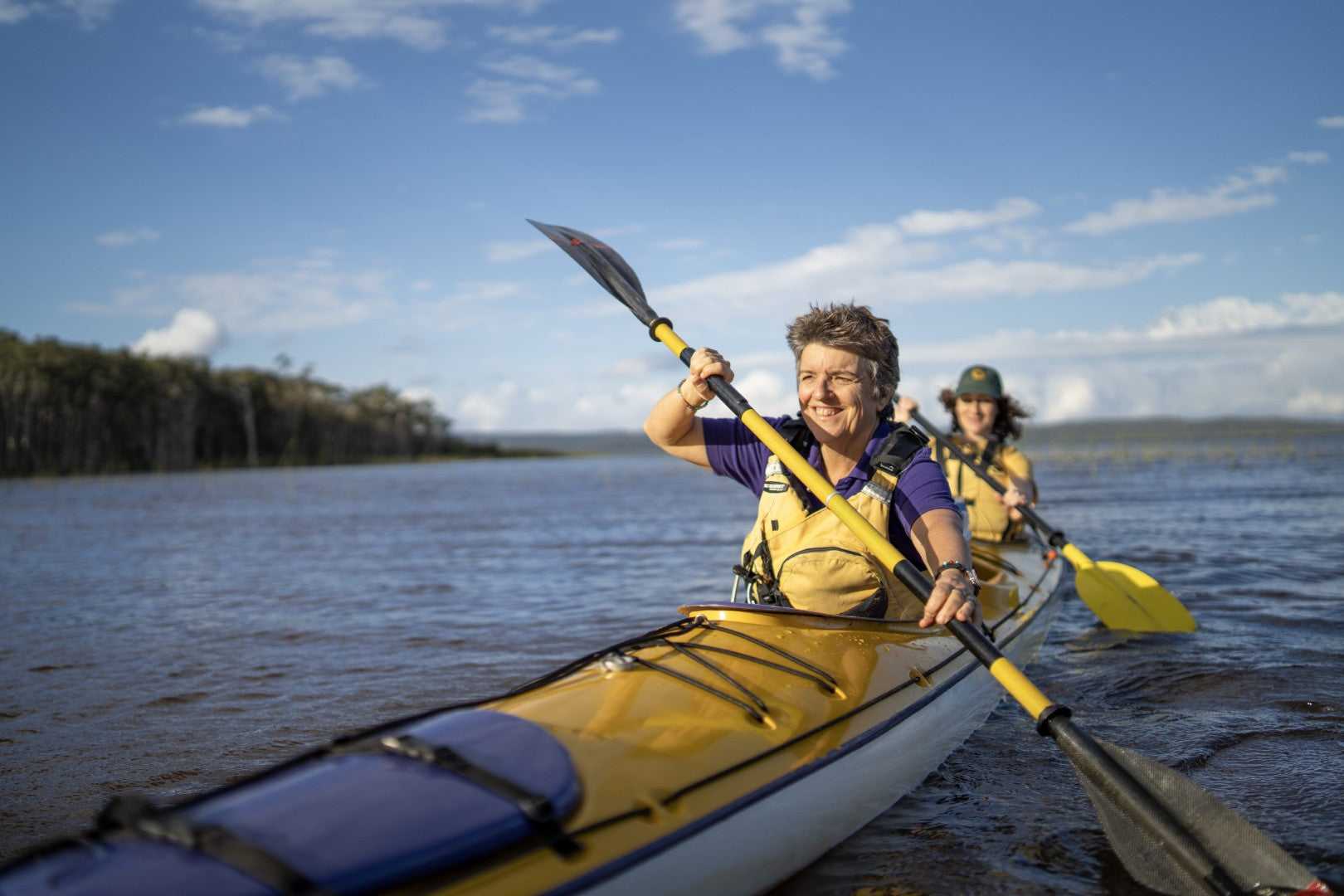 Travelers kayaking on K'gari lake during East Coast Australia tour. Outdoor adventure on 8-day Sydney to Brisbane journey.
