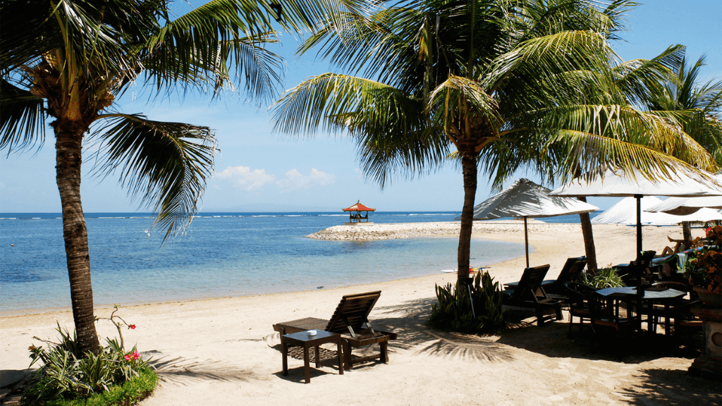 Beachfront resort with palm trees and lounge chairs, offering relaxation in Bali Komodo Lombok Tours - Explore Culture & Nature.