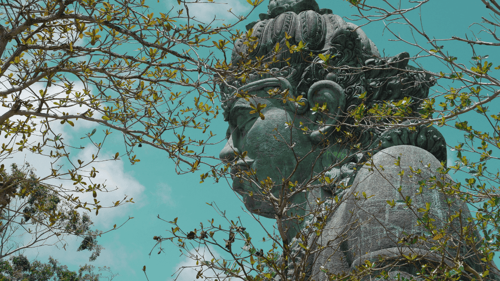 Statue of a Balinese deity partially hidden by branches, representing spirituality in Bali Komodo Lombok Tours - Explore Culture & Nature.