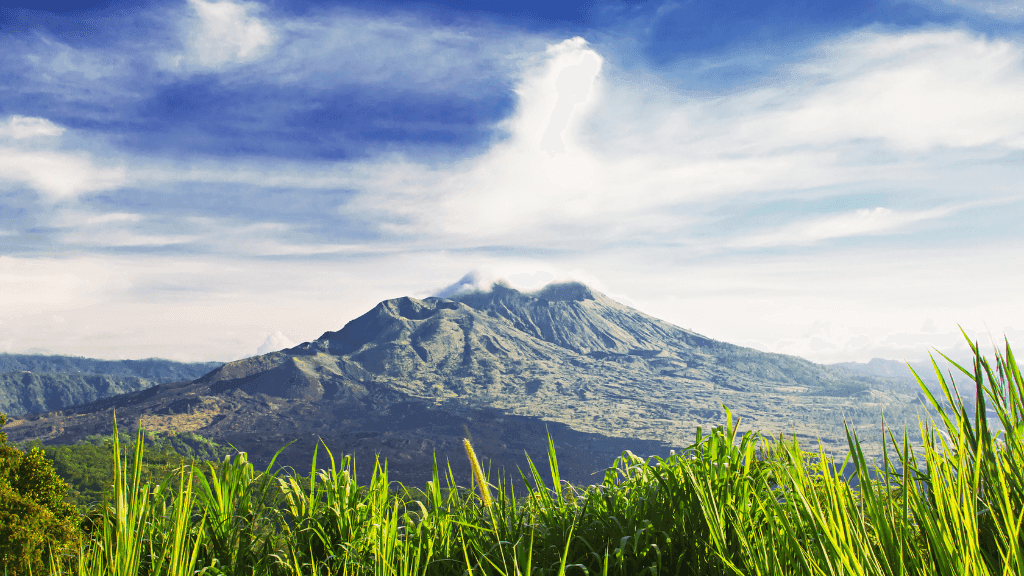 Mount Batur volcano under a blue sky, a natural wonder included in Bali Komodo Lombok Tours - Explore Culture & Nature.