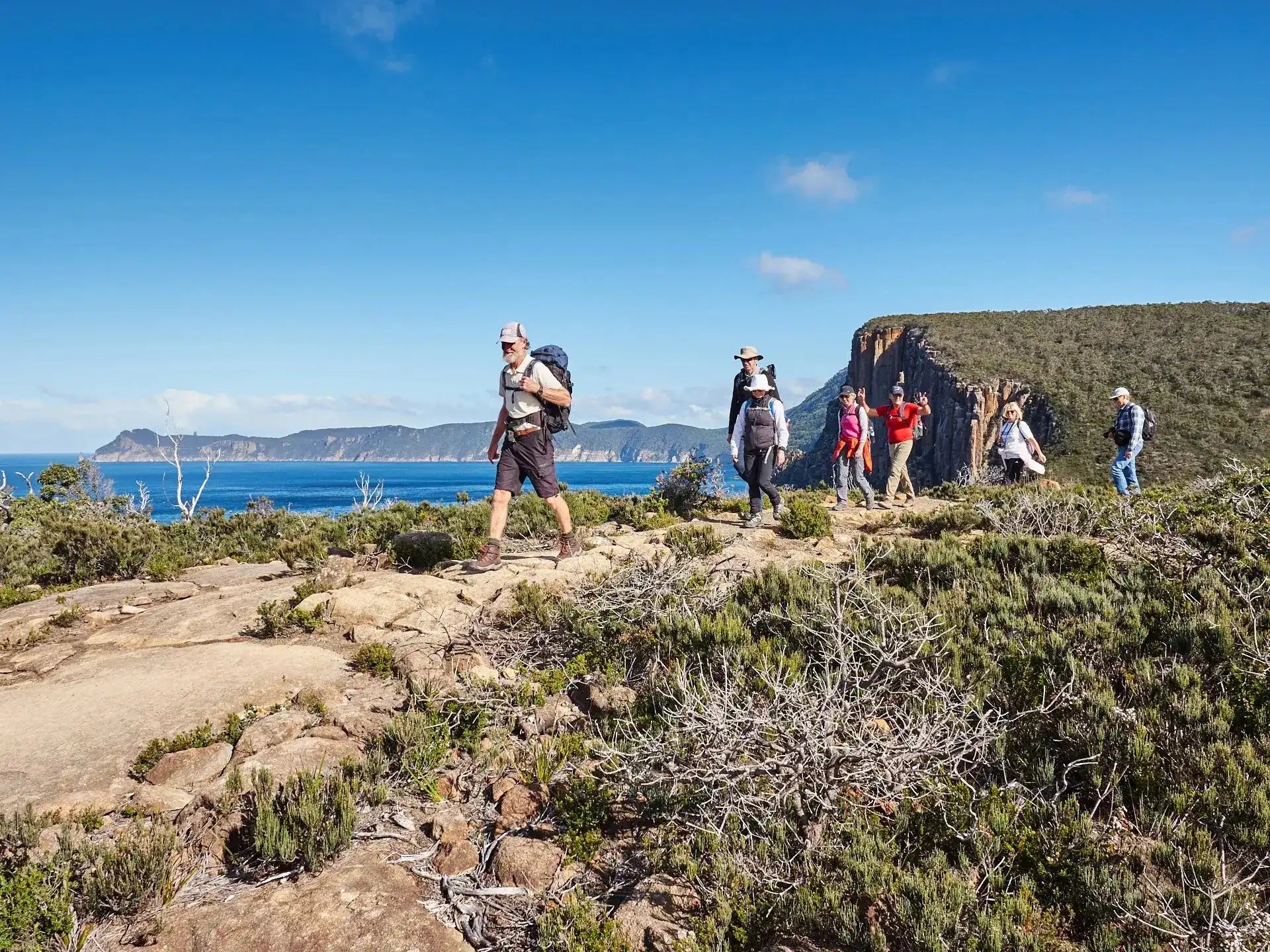 Group of hikers on a rocky trail with ocean and cliffs in the background