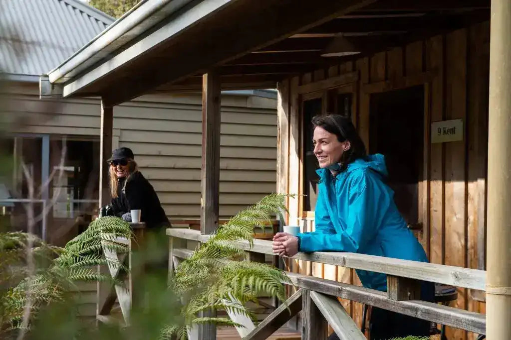 Two people on a wooden veranda with a rustic cabin in the background