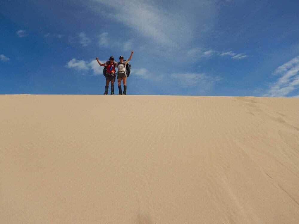 Two hikers celebrating atop a sand dune under blue sky during the 4-Day Ningaloo Kayak Expedition - Trek & Camp Adventure.