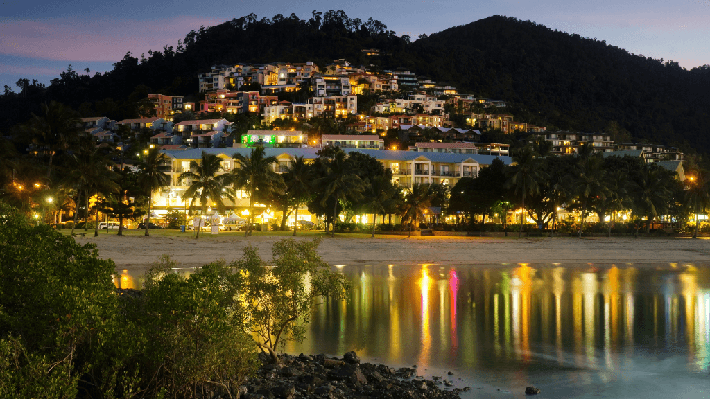 Airlie Beach waterfront at night with lights reflecting on water, part of East Coast Adventure 14/16-Day Small-Group Tour. Vibrant nightlife scene.