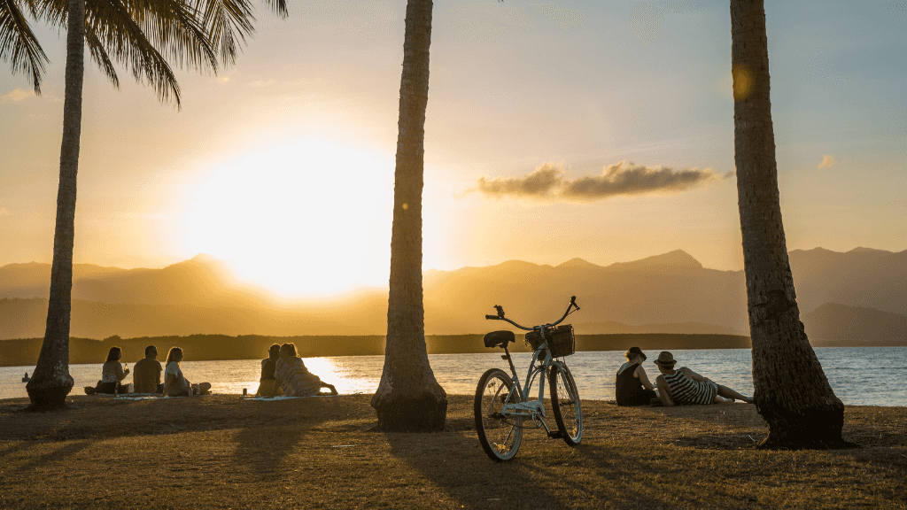 People relaxing under palm trees at sunset in Port Douglas on East Coast Adventure 14/16-Day Small-Group Tour. Scenic tropical beach destination.
