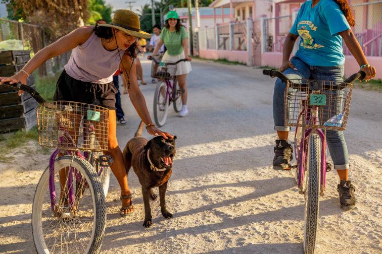 Travelers biking through a village and petting a dog, showcasing local interaction on the 32-Day Mexico to Costa Rica Adventure - Small Group Tour.