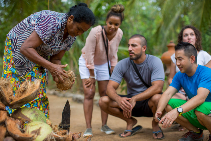 Local woman demonstrating coconut preparation to travelers. Explore Sri Lanka - Land & Sea Tour Options includes hands-on cultural activities.
