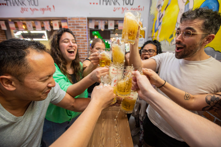 Group toasting with Vietnamese beer at a local bar. Social and cultural experience on Vietnam Hiking and Cycling Tour.