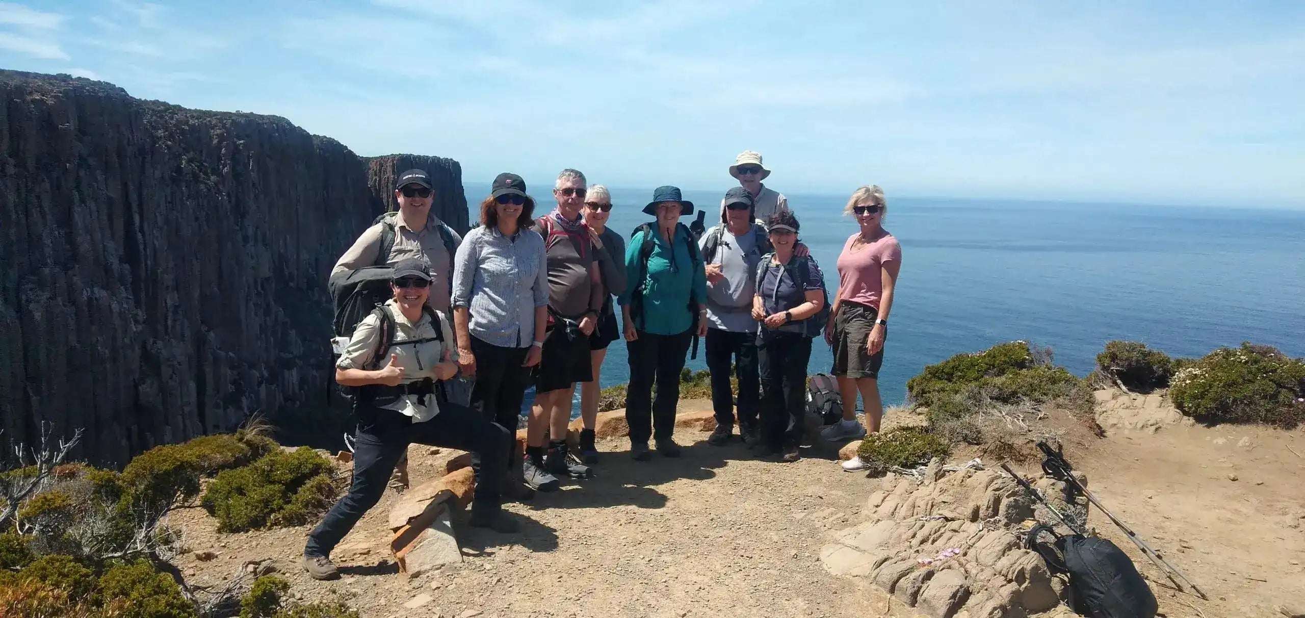 Group of people posing for a photo on a rocky outcrop with ocean and sky in the background