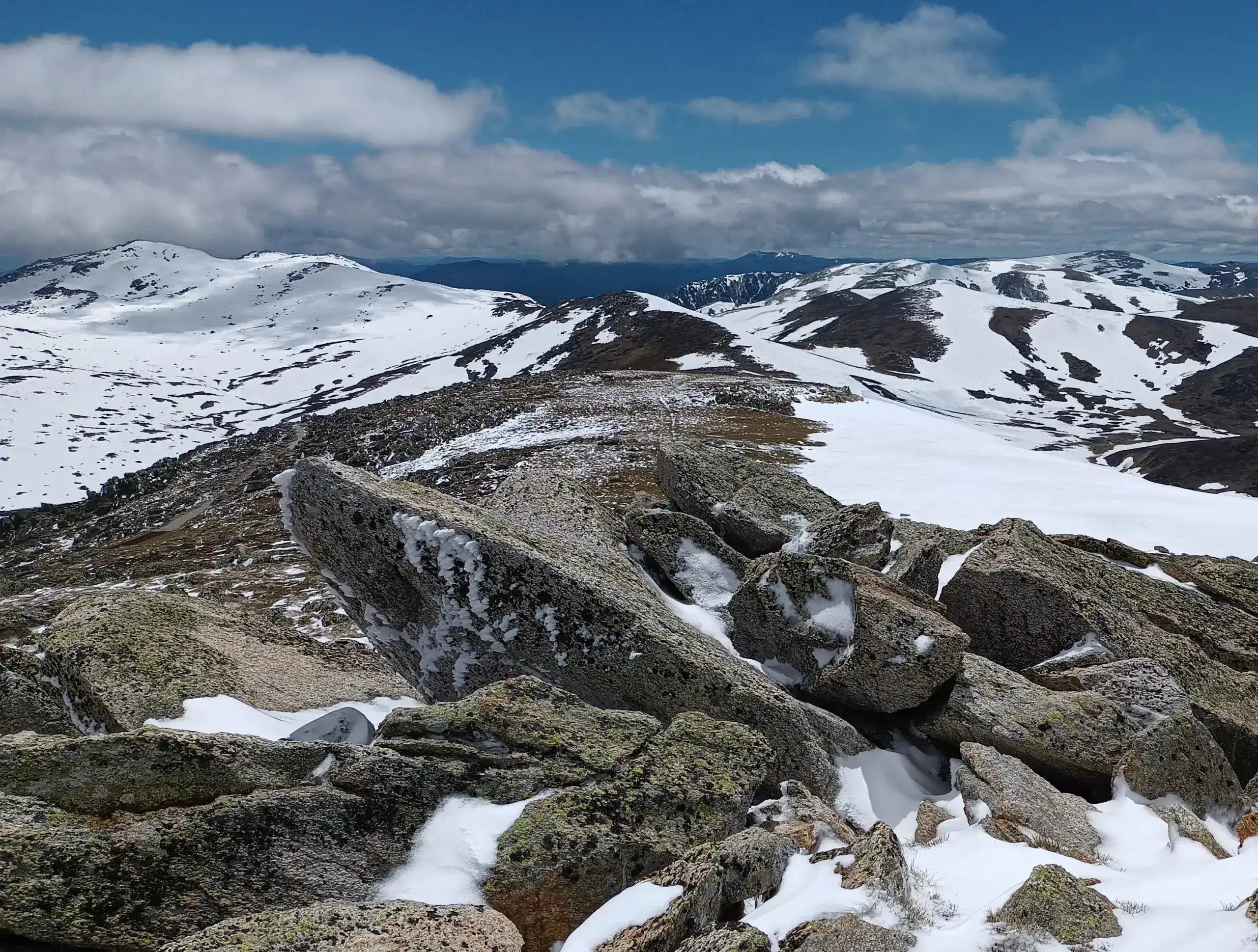 Rugged mountain landscape with snow and rocks under a blue sky with clouds.