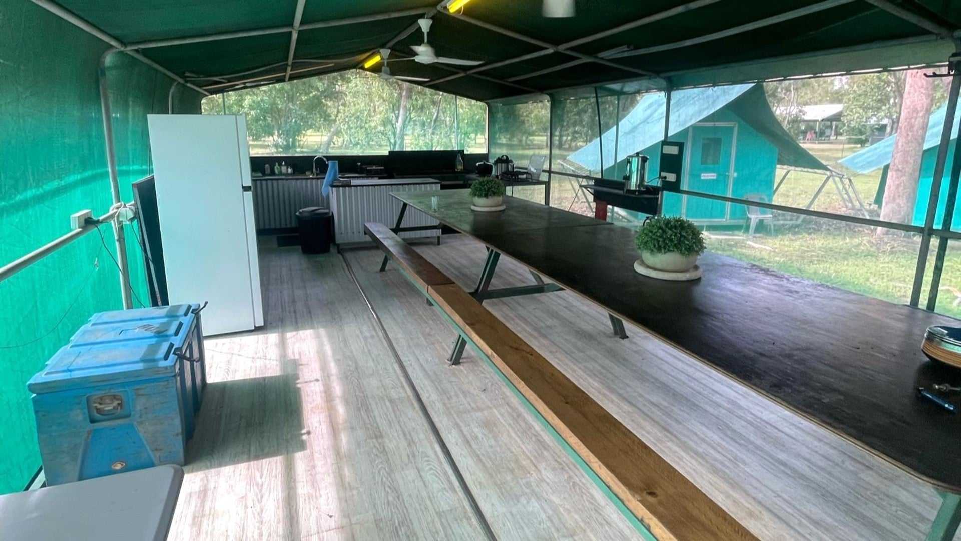 Camp kitchen setup at Kakadu Litchfield Camping Adventure - 3-Day Tour. Covered dining area with long table and green tents in background.