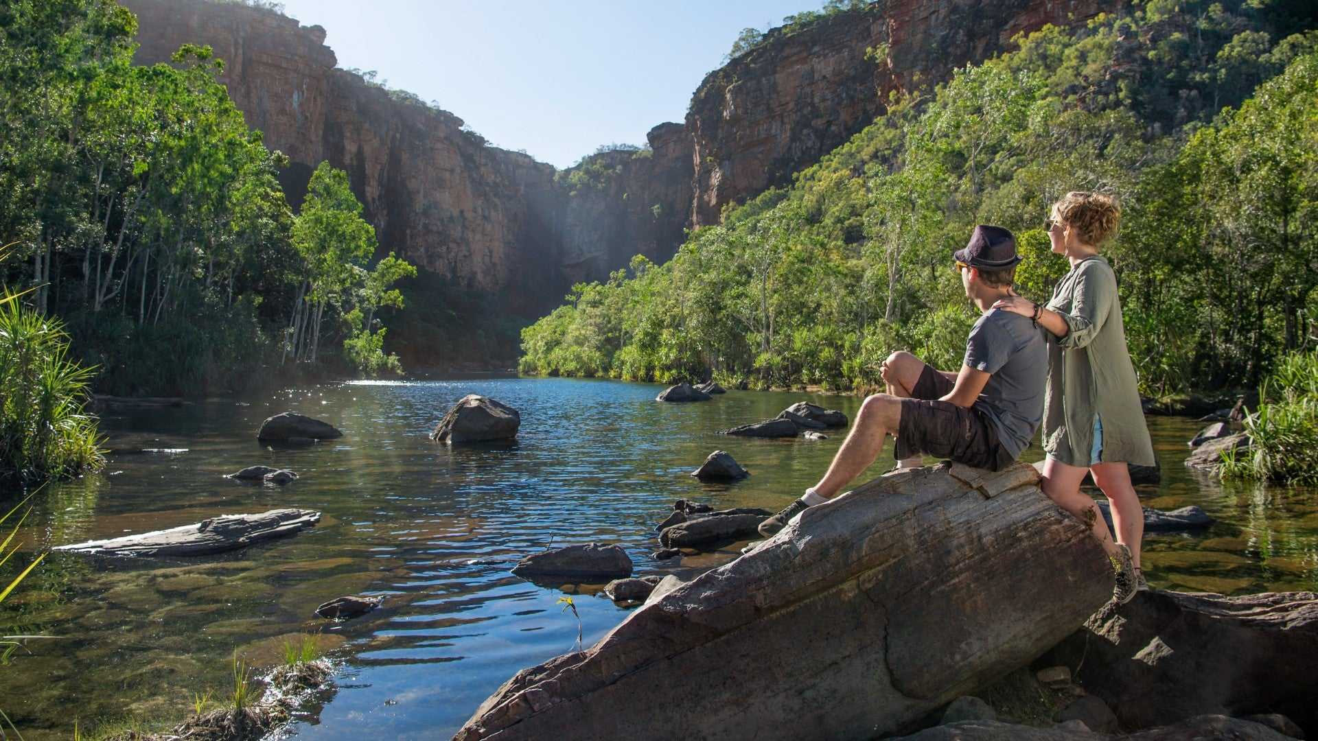 Couple enjoying serene gorge view at Kakadu Litchfield Camping Adventure - 3-Day Tour. Scenic rock pool surrounded by lush cliffs and forest.