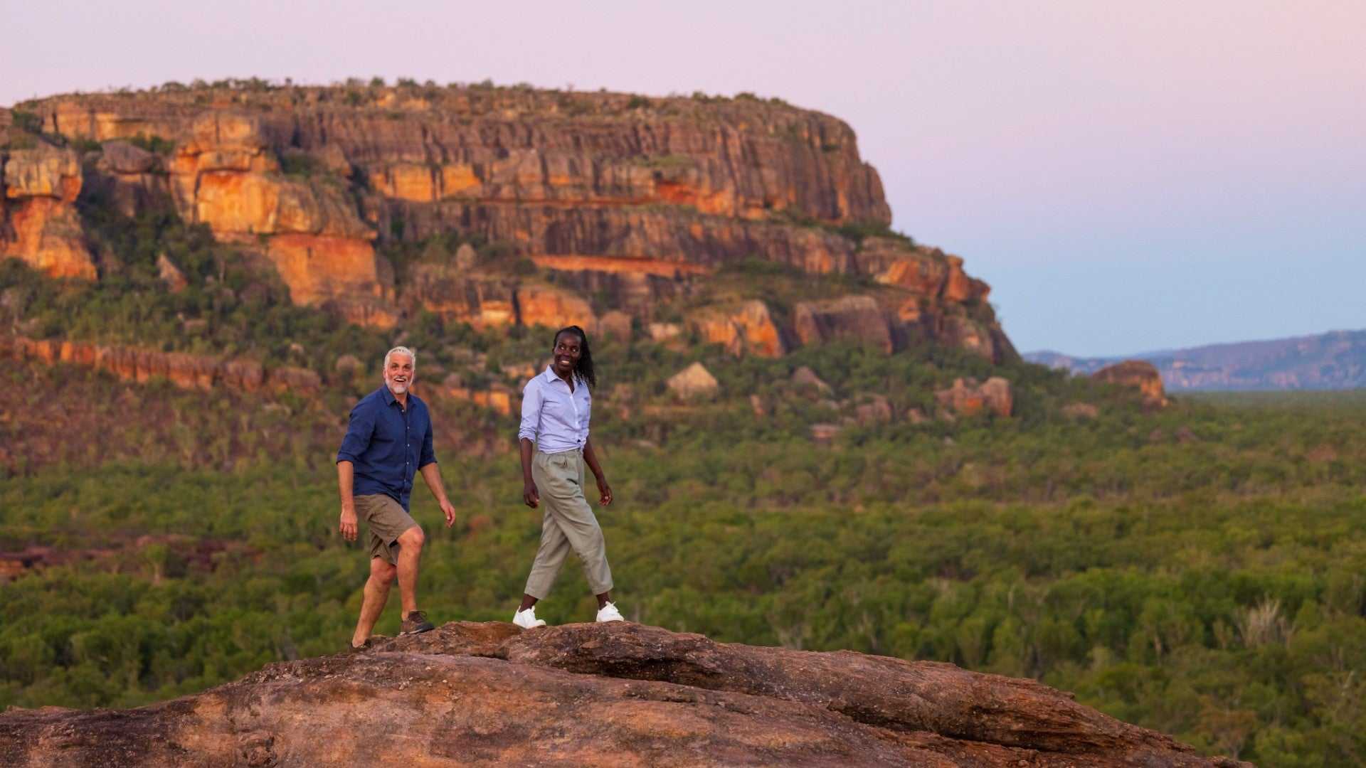 Couple hiking near sandstone cliffs in Kakadu on Kakadu Katherine Gorge Tour | 4-Day Comfort Travel. Explore ancient landscapes and rock formations.