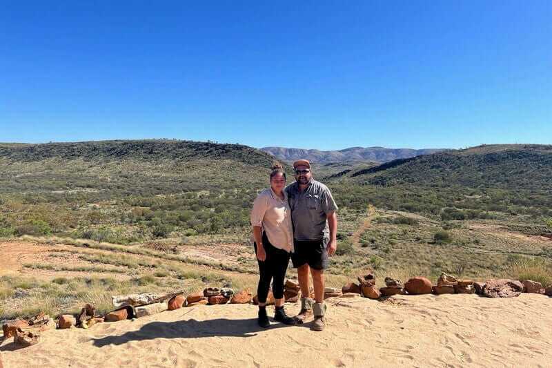 Two hikers standing on sandy lookout with mountain views, part of Larapinta Trail 5-Day Expedition in Australia’s outback.