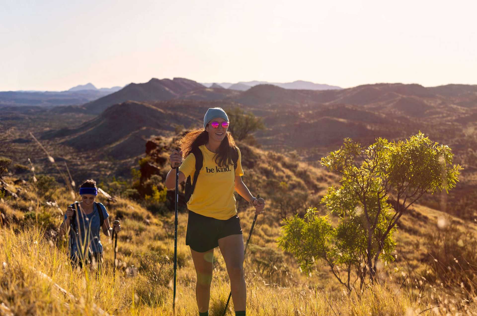 Woman hiking with trekking poles on grassy ridge during Larapinta Trail 5-Day Expedition, perfect for moderate adventure seekers.