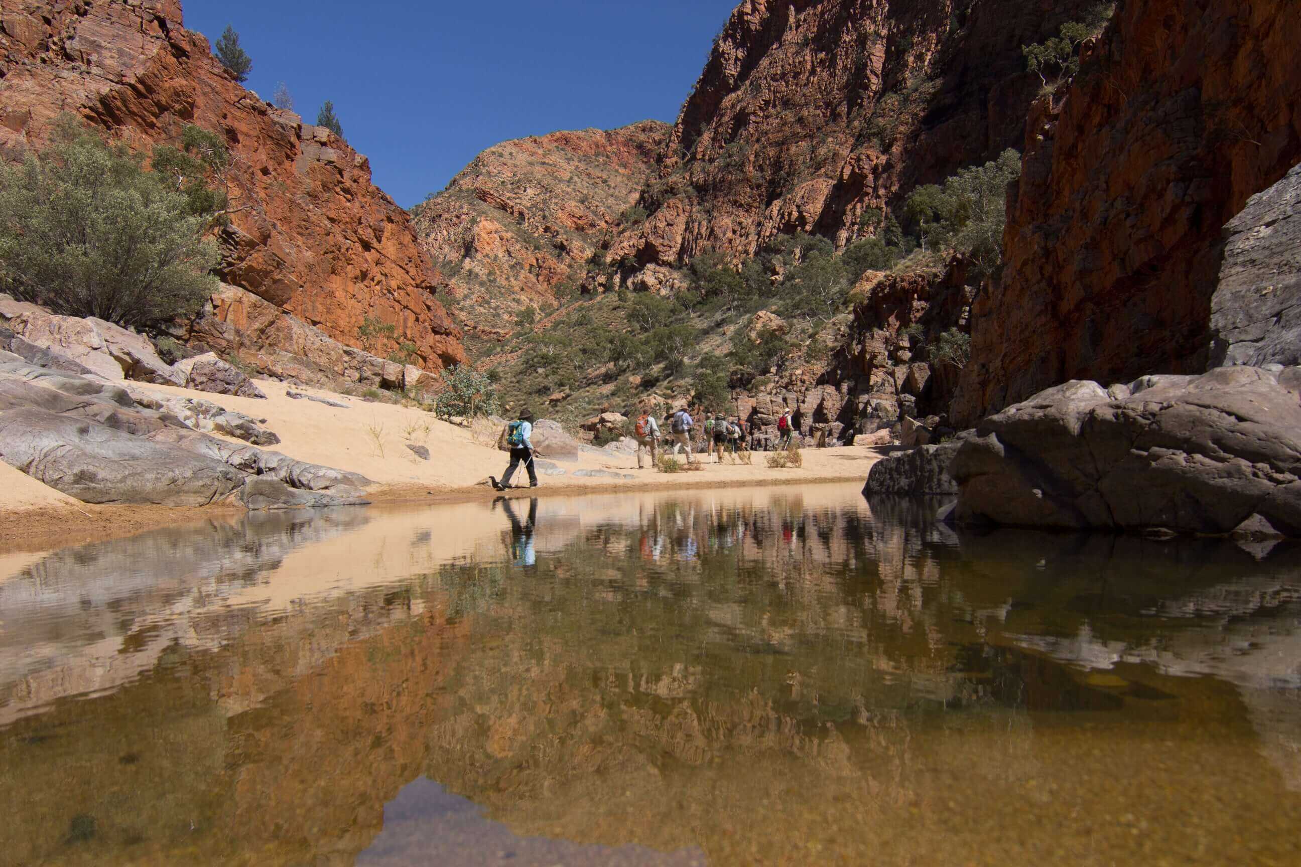 Hikers crossing shallow creek in rocky gorge, part of the immersive Larapinta Trail 5-Day Expedition in West MacDonnell Ranges.