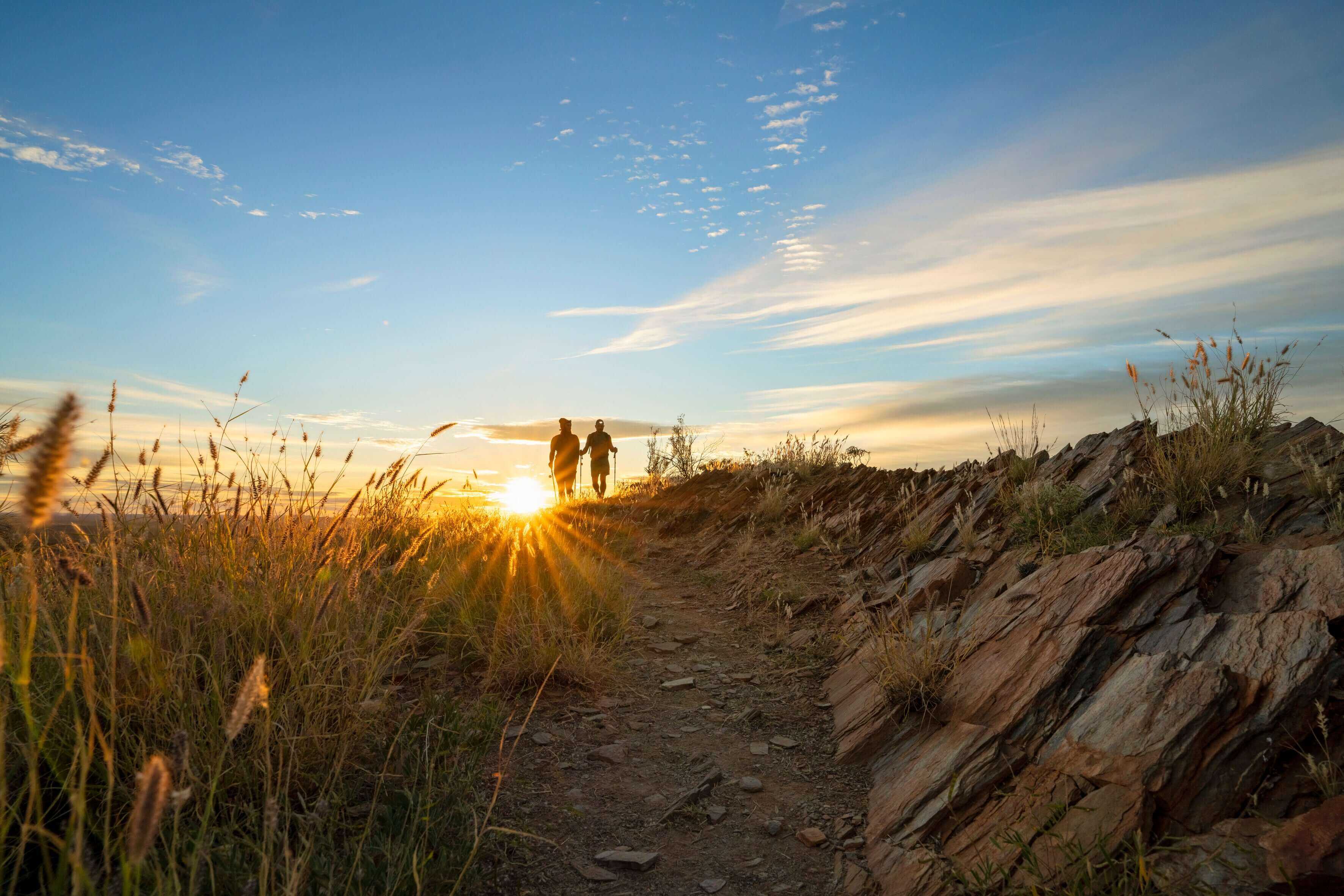Couple walking into sunset on rocky trail, a romantic moment on Larapinta Trail 5-Day Expedition in West MacDonnell Ranges.