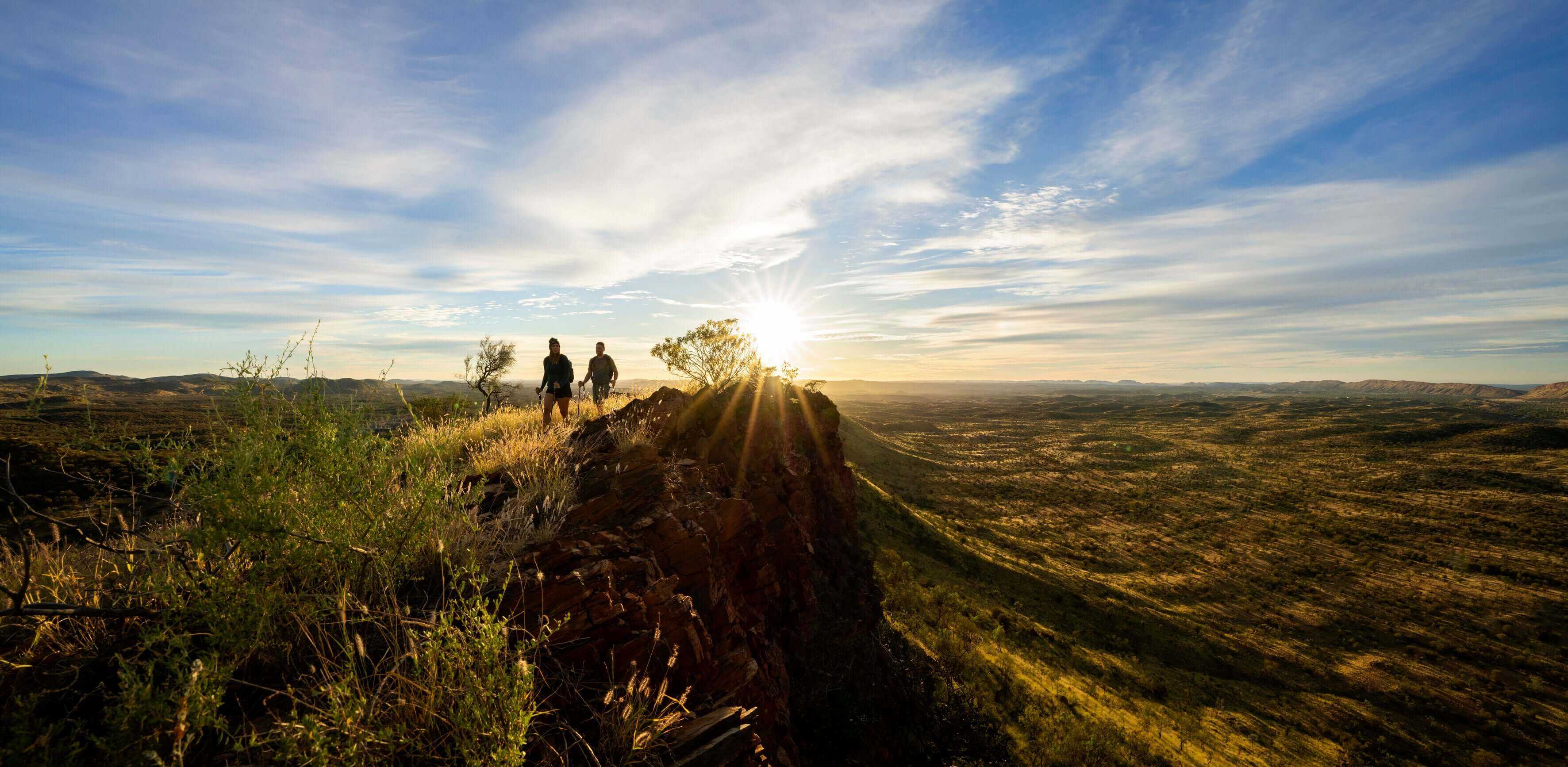 Three hikers on ridge at sunrise, enjoying panoramic views on Larapinta Trail 5-Day Expedition in West MacDonnell Ranges.