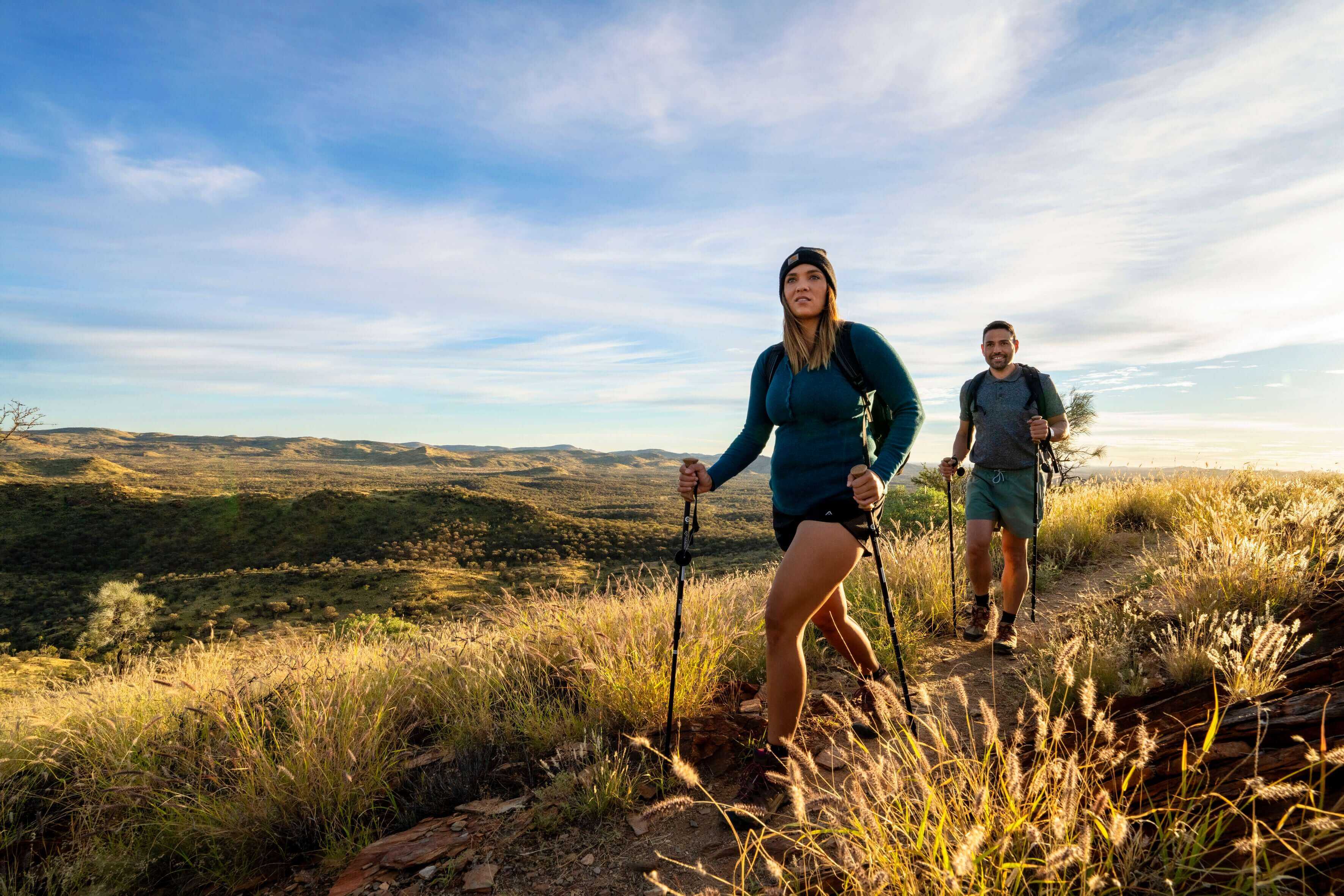 Two hikers trekking through golden grasslands on Larapinta Trail 5-Day Expedition, part of iconic outdoor adventure in Australia.