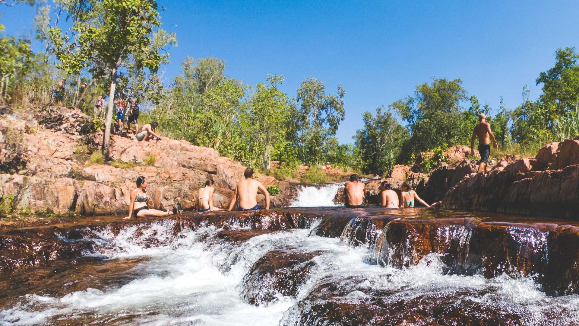 Group enjoying natural rock spa at Kakadu Litchfield Camping Adventure - 3-Day Tour. Clear water flowing through red stone pools.