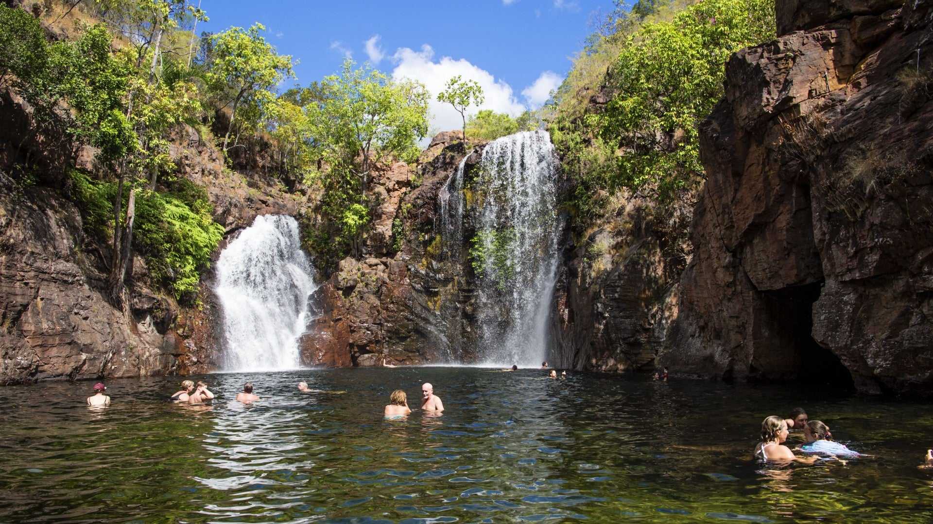 Travelers swimming at twin waterfalls during Kakadu Litchfield Camping Adventure - 3-Day Tour. Scenic natural pool surrounded by cliffs.