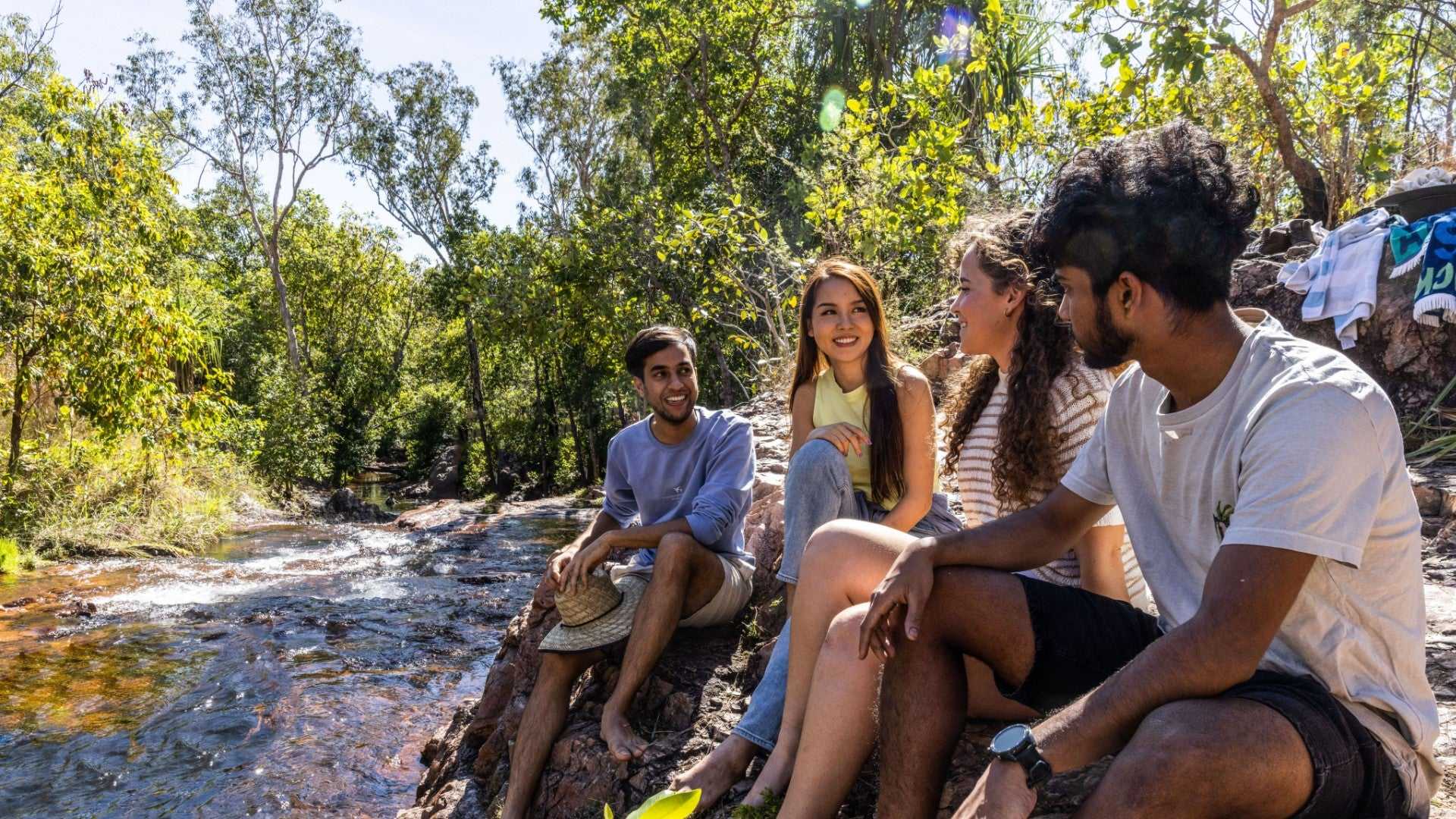 Group of friends relaxing by forest stream at Kakadu Litchfield Camping Adventure - 3-Day Tour. Social moment in lush, shaded environment.