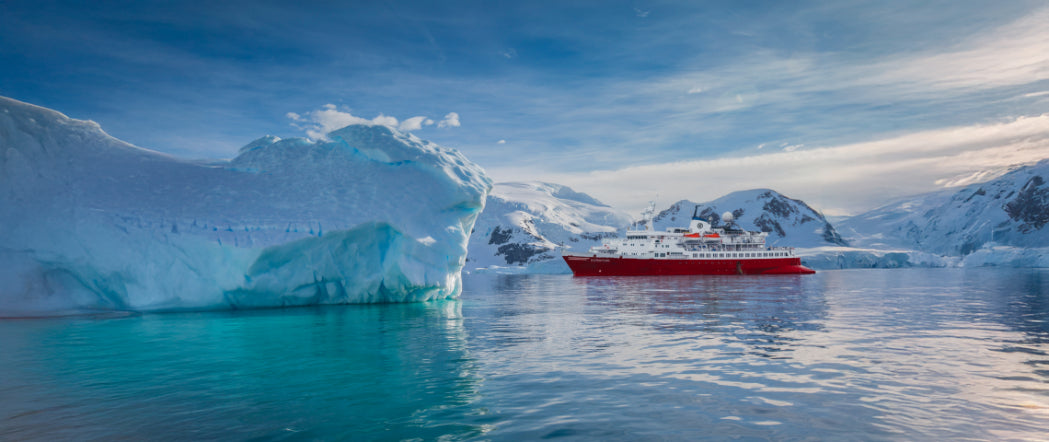 Red expedition cruise ship sails past massive iceberg in Antarctica on 11-day Antarctica Expedition Cruise - Edge of the Earth.