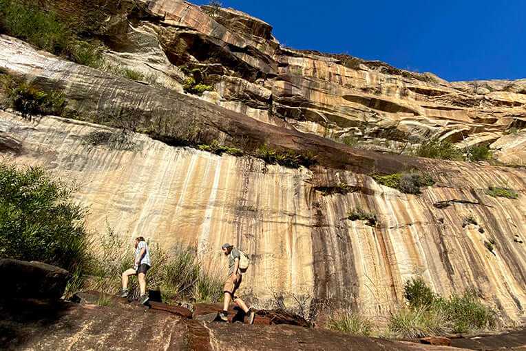 Adventurers hiking rocky terrain under towering sandstone cliffs on a guided tour in the Grampians.
