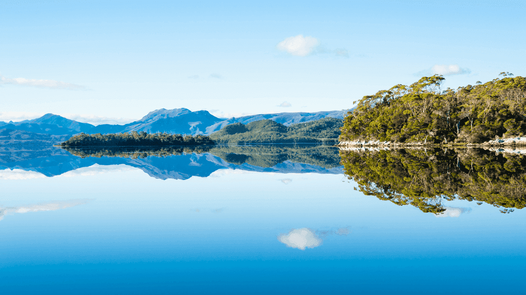 Glass-like reflections of Tasmanian forest and mountains on a calm lake, featured in the 8-day sea kayak and nature exploration tour.