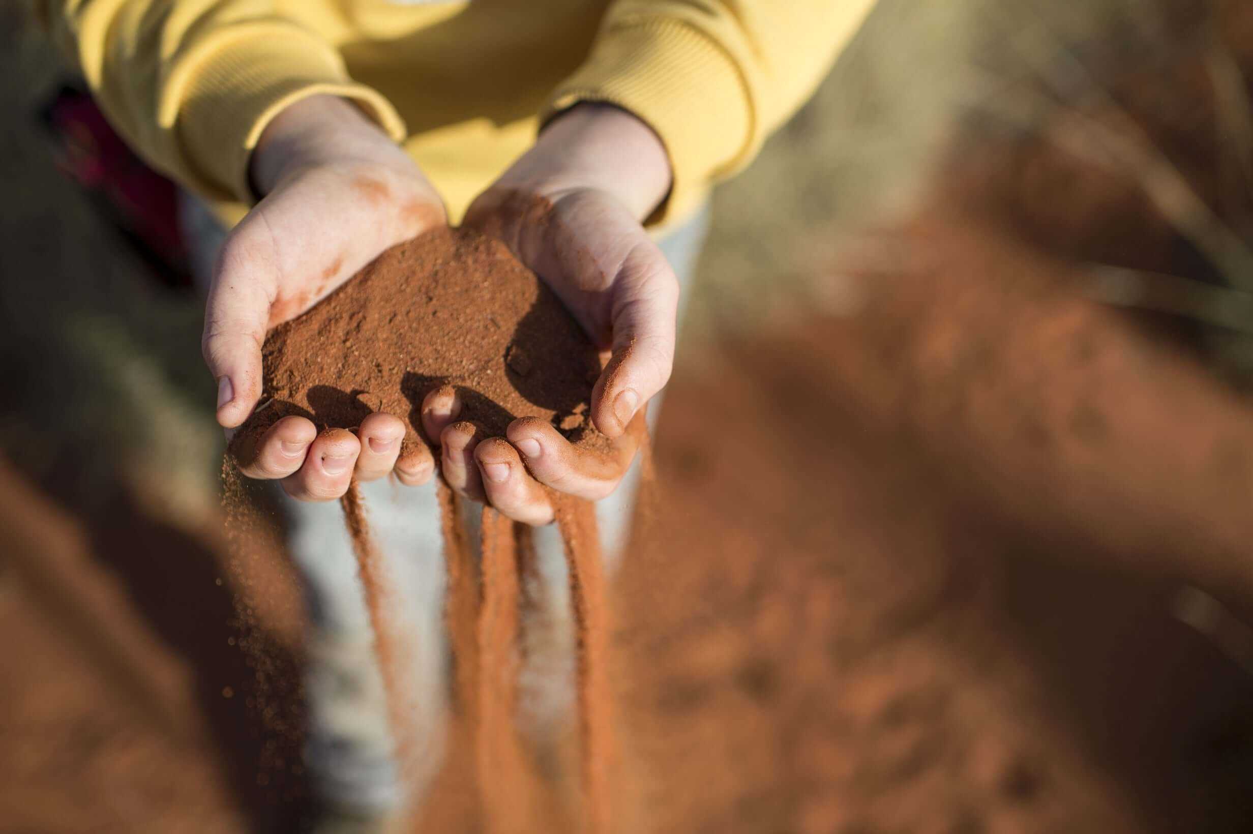 Hands holding red desert sand, symbolizing connection to nature on Larapinta Trail 5-Day Expedition in West MacDonnell Ranges.