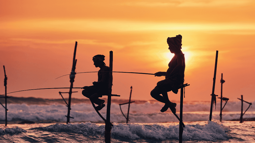 Silhouetted stilt fishermen at sunset on Sri Lanka's coast, a cultural experience on the 12-day spice gardens and beach tour.