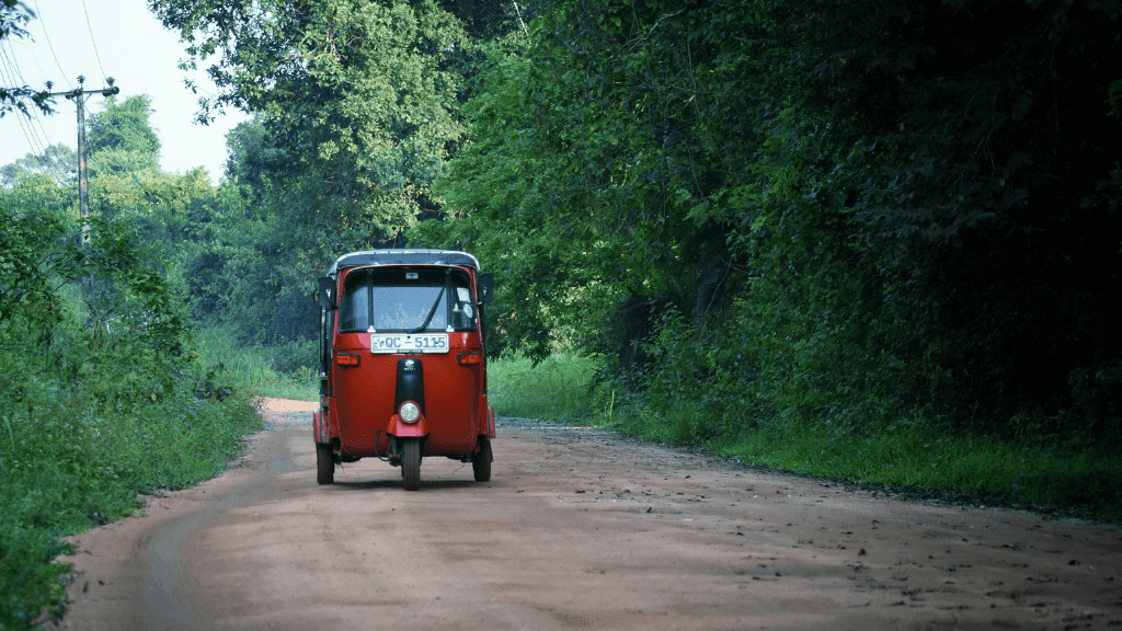 Red tuk-tuk driving on a dirt road through lush forest, part of the local travel experience on the 12-day Sri Lanka tour.