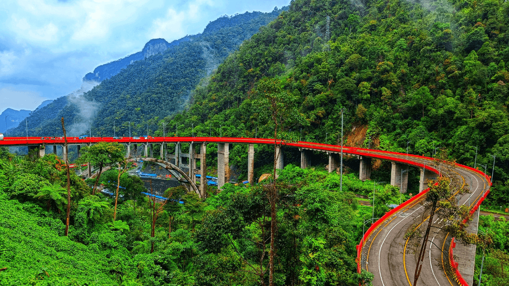 Winding red bridge through lush Sumatran mountains, a scenic route on the Jungle River Expedition adventure tour.